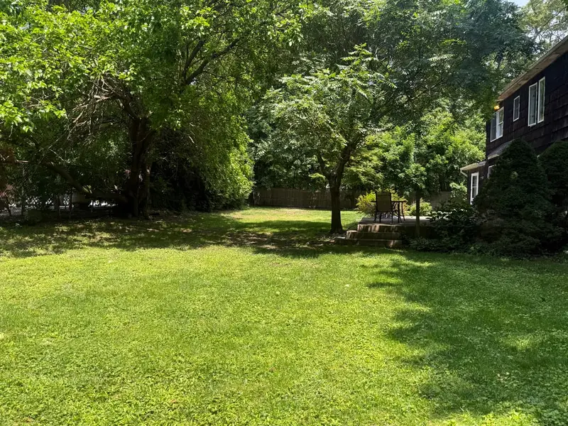 Shaded backyard lawn beside a dark shingled colonial, Smithtown, NY